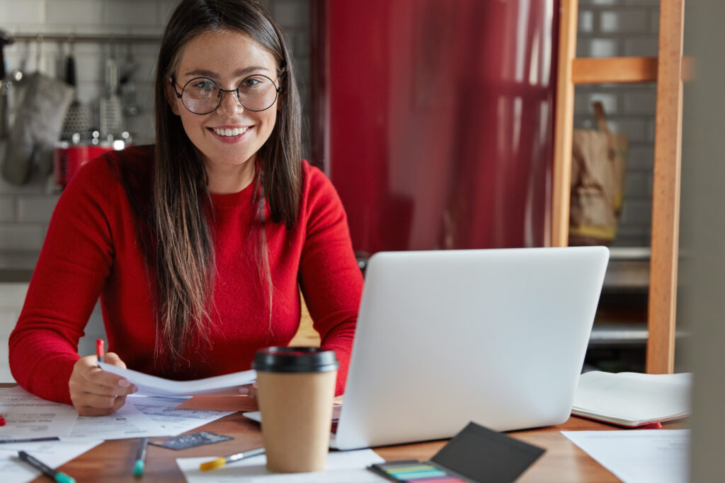 glad student prepares for seminar, writes down homework checks text documentation, uses laptop computer, sits at kitchen table with cozy interior, enjoys takeaway coffee, checks delivered bills ExpressNIE is the most trusted source for getting your Spanish NIE fast. Call today!